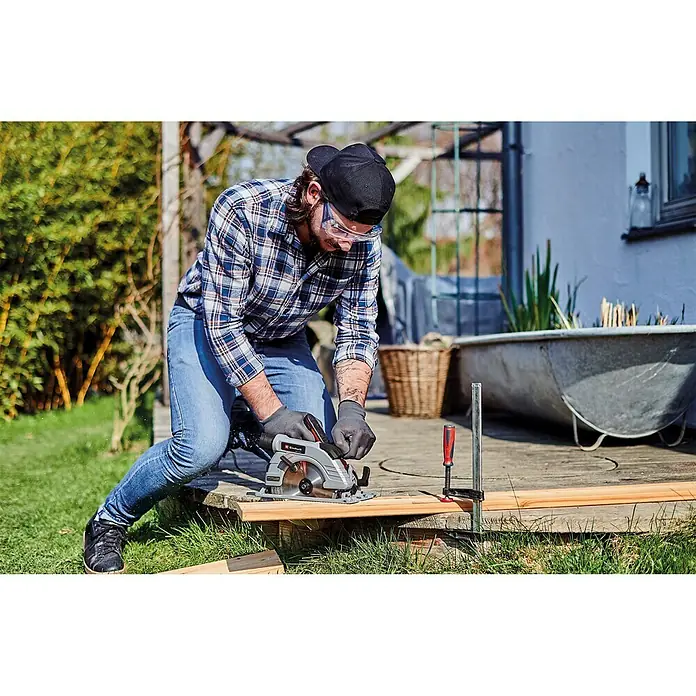 Einhell Professional Power X-Change 18V Akku-Handkreissäge TE-CS 18/190 Li BL-Solo - 18 V, Ohne Akku, Leerlaufdrehzahl: 0 U/min - 3.800 U/min - Ein Mann mit Schutzbrille und Handschuhen sägt ein Holzbrett mit einer Einhell Handkreissäge im Garten.