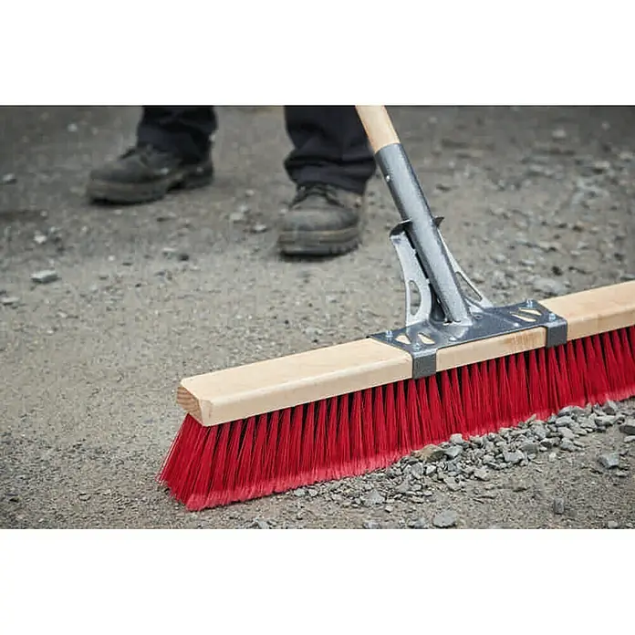 Freund Victoria Straßenbesen ProfiArbeitsbreite: 60 cm, Material Borsten: Elaston, Rot, Natur - Nahaufnahme einer roten Straßenbürste mit Holzrücken und silberner Halterung, die auf einem unebenen Untergrund steht.