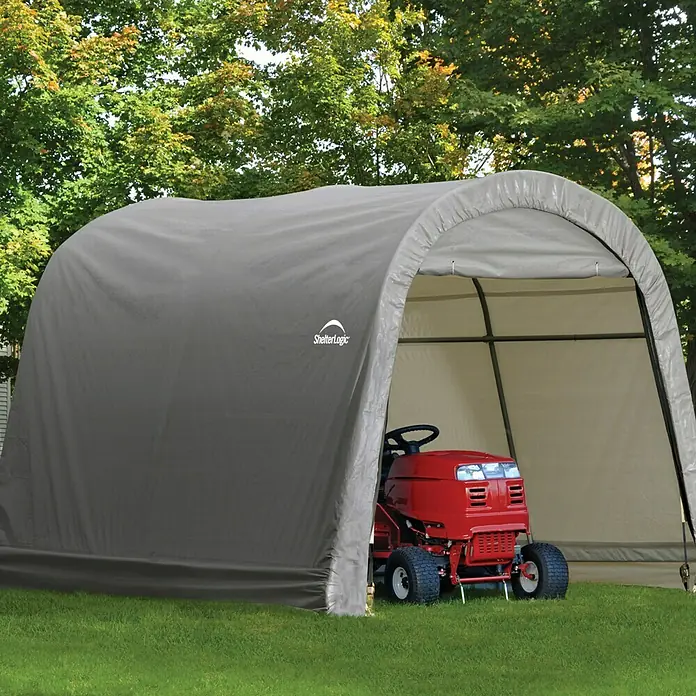 ShelterLogic Gerätehaus - Außenbreite inkl. Dachüberstand: 300 cm, Außentiefe inkl. Dachüberstand: 300 cm, Stahl, Grau - Eine ShelterLogic-Lagerzelthalle mit einem roten Rasentraktor im Inneren, umgeben von grünen Bäumen und Gras.