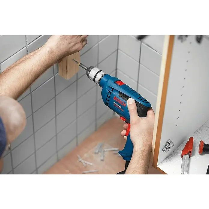 Bosch Professional Schlagbohrmaschine GSB 13 RE - 600 W, Schnellspannbohrfutter - Ein Mann bohrt mit einer blauen Bosch GSB 13 RE Professional Bohrmaschine ein Loch in ein Holzstück. Das Werkzeug ist gut sichtbar.