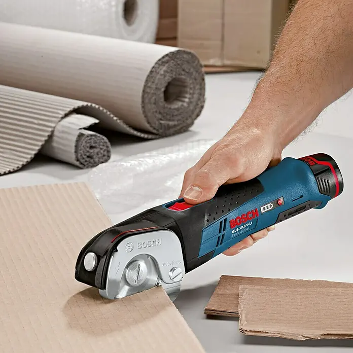 Bosch Professional Akku-Universalschere GUS 12V-300 - 12 V, Li-Ionen, Ohne Akku, Geeignet für: Materialien bis 11 mm Stärke - Das Bild zeigt einen Bosch Akku-Universalschneider GUS 10,8 V-LI Professional im Einsatz mit einer Hand, der Karton schneidet.