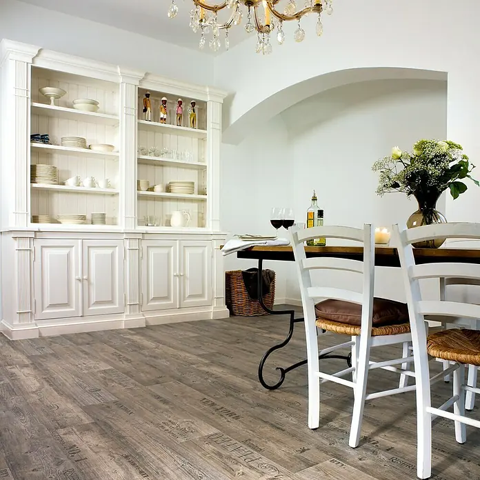 CV-Boden Meterware Memphis - 400 cm, Vino, Grau - Ein einladender Essbereich mit einem rustikalen Holztisch, umgeben von weißen Stühlen, und einem eleganten Bücherregal im Hintergrund.