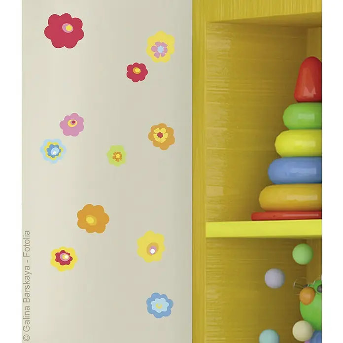 Vinilo de pared - Flores de colores, Multicolor, Plástico - Estantería amarilla con juguetes coloridos como una torre apilable y una figura verde. La pared está decorada con pegatinas de flores.