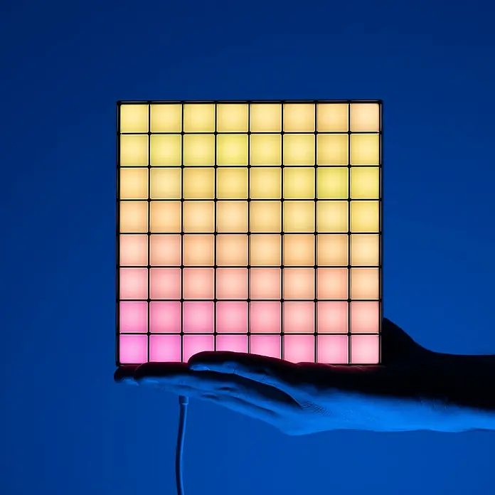 Twinkly LED-Panel-Set Squares RGB Starterset - RGB - Ein leuchtender LED-Controller mit einem Raster aus gelben, pfirsichfarbenen und pinken Pads in der Hand, ideal für Musikproduktion und kreative Lichtshows.