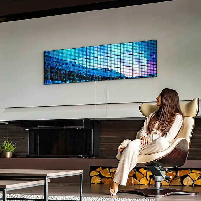 Twinkly LED-Panel-Set Squares RGB Starterset - RGB - Eine Frau entspannt sich in einem Sessel vor einem grossen Samsung The Wall Micro LED-Display, das an der Wand hängt.