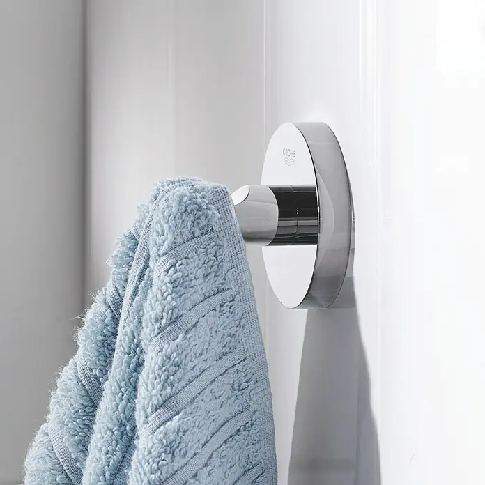 Grohe Essentials Bademantelhaken - Chrom, Glänzend - Nahaufnahme des Grohe Essentials Handtuchhalters mit einem blauen Handtuch daran, montiert an einer weißen Wand im Badezimmer.