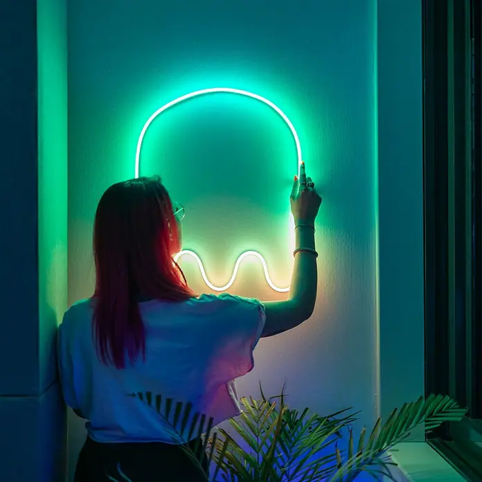 Twinkly LED-Lichtschlauch Flex - Länge: 2 m, Lichtfarbe: RGB, 15 W - Die Frau berührt eine grüne Geister-Neonleuchte an der Wand, die eine geheimnisvolle und spielerische Atmosphäre schafft.