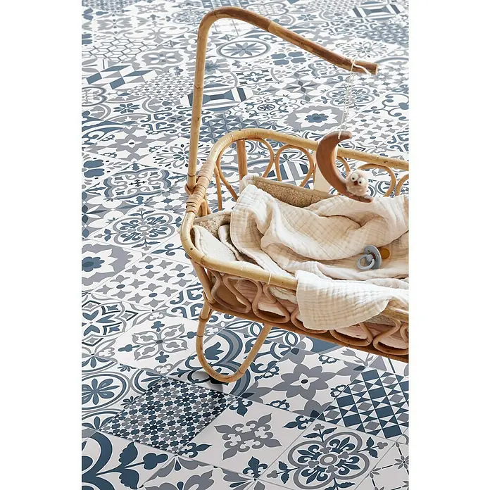 Beauflor PVC-Boden Meterware Feelings - Sonstige, Breite: 300 cm, Blau/Grau - Nahaufnahme eines dekorativen Korbbettchens mit Spielzeug und Decken auf einem blauen und grauen Bodenfliesenmuster.
