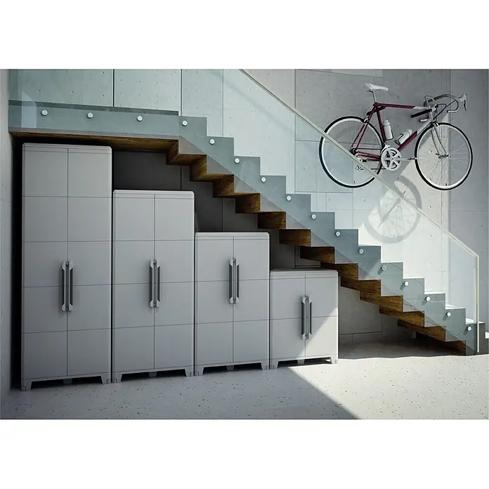 Terry Transforming Ampliación armario de PVC Modular - L x An x Al: 43,6 x 78 x 41,4 cm - Un conjunto de armarios grises de diferentes alturas debajo de una escalera de madera, con una bicicleta colgada en la pared al lado.