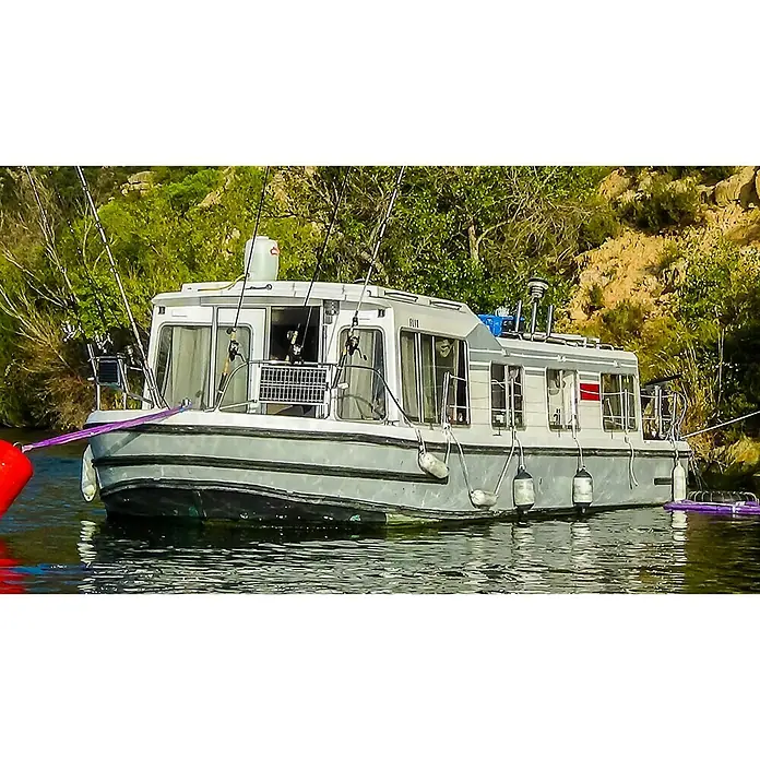 Sunset Solarmodul-Set Laminat - Nennleistung: 10 W, Für Booten, Yachten und Wohnmobilen - Ein graues Hausboot mit Fischruten, das auf dem Wasser treibt und von grüner Vegetation umgeben ist.