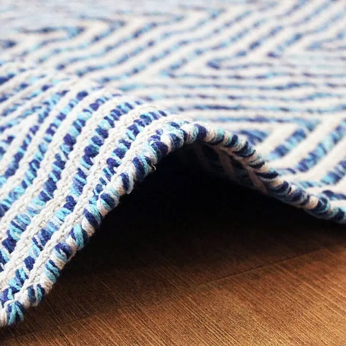 Kayoom Flachgewebeteppich Cocktail 400 - Blau, 230 x 160 cm, 100% Baumwolle - Nahaufnahme eines blauen und weißen gewebten Teppichs mit geometrischem Muster auf einem Holzboden.