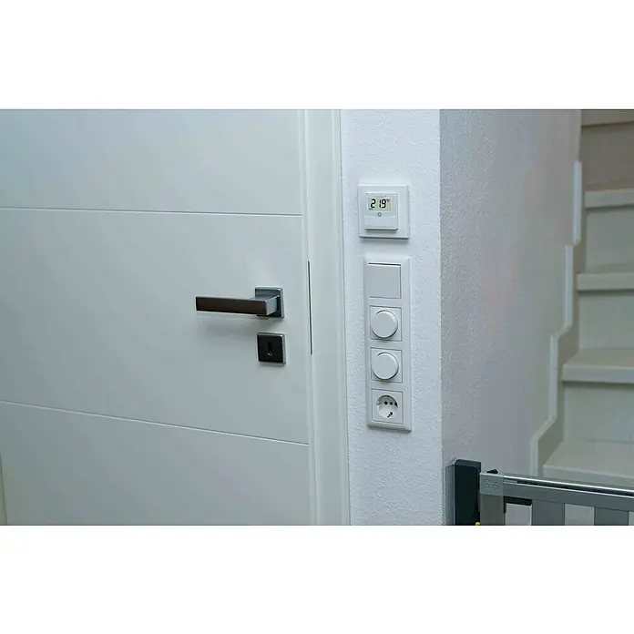 Homematic IP Funk-Raumthermostat HmIP-BWTH - Netzbetrieben, 230 V, 54 x 86 x 86 mm, Weiß - Nahaufnahme einer weißen Tür mit einem modernen Türgriff, neben einer Wand mit Thermostat, Schaltern und einer Steckdose.