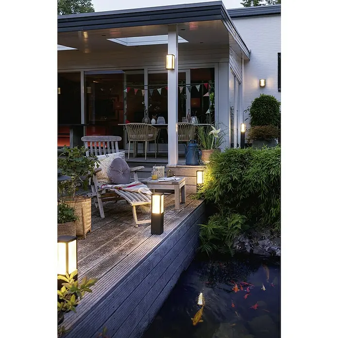Philips Hue LED-Außenwandleuchte Impress - 8 W, 14,1 x 12 x 24 cm, Schwarz, IP44 - Diese Aufnahme zeigt Außenleuchten, die eine gemütliche Atmosphäre auf einer Terrasse mit Teich erzeugen. Das warme Licht betont die Gartenarchitektur.