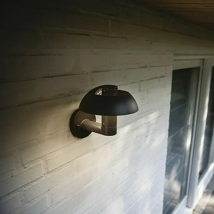 Lutec Aplique exterior LED Spril - 8,4 W, 22,7 x 19 x 20 cm, Antracita, IP54 - Lámpara de pared exterior con pantalla negra y brazo de metal en una pared de ladrillo blanco. Diseño simple para exteriores.