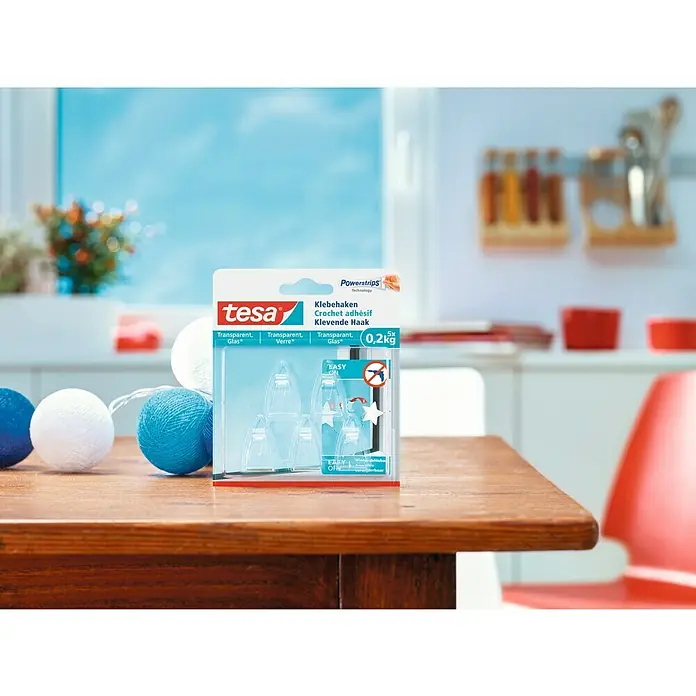 Tesa Colgador adhesivo - Transparente, Carga soportada: 0,2 kg, 5 ud. - La imagen muestra un paquete de ganchos adhesivos Tesa Powerstrips, transparentes y aptos para una carga de hasta 0,2 kg.