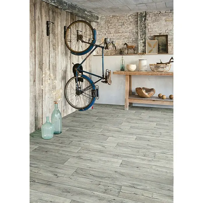 Beauflor PVC-Boden Meterware Feelings - 200 cm, Cracked Oak, Grau - Zimmer mit grauem Holzboden, an der Wand ein Fahrrad. Der graue Holzboden verleiht dem Raum ein modernes und stilvolles Aussehen.