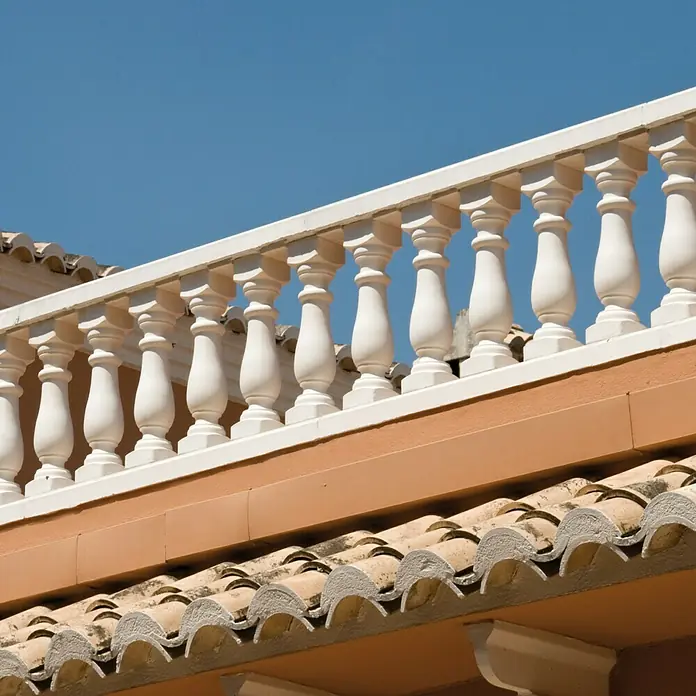 Pasamano Palermo - Hormigón - Vista detallada de un edificio con tejas de terracota y una barandilla de balaustres blanca contra un cielo azul claro.