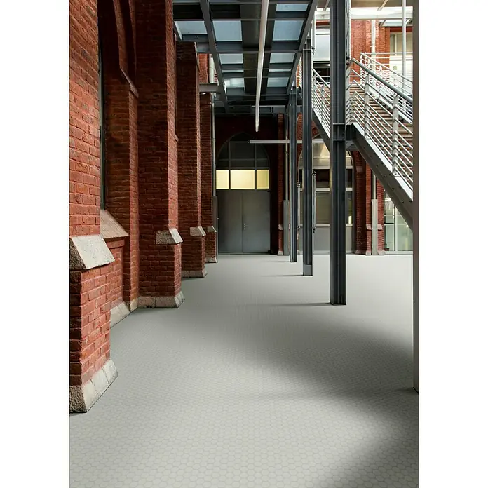 Beauflor PVC-Boden Meterware Novo - 200 cm, Solid Disc, Grau - Innenaufnahme eines Gebäudes mit grauem Sechskantfliesenboden und roter Backsteinarchitektur mit Stahlstützen.