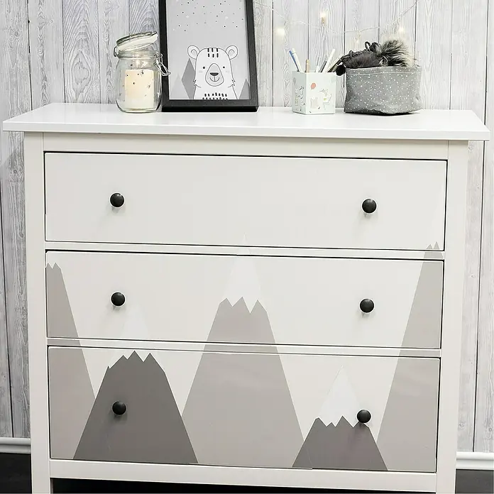 D-c-fix Klebefolie Uni Seidenmatt - 200 x 45 cm, Weiß, Selbstklebend - Eine moderne, weiße Kommode mit drei Schubladen, verziert mit einem stilvollen Bergmotiv in Grauabstufungen, ideal für jedes Kinderzimmer.