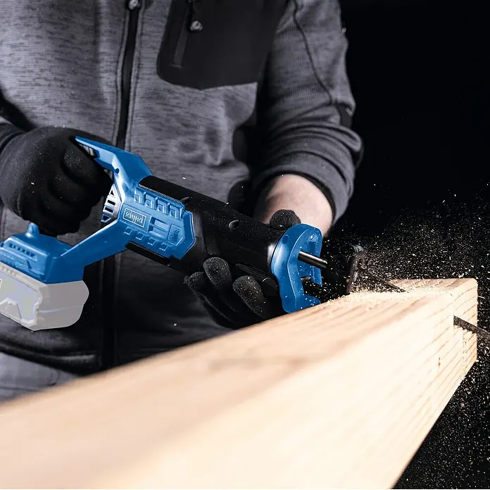 Scheppach IXES 20V Akku-Säbelsäge BC-RS250-X - 20 V, Hublänge: 28 mm - Akkubetriebene Säbelsäge im Einsatz: Das blaue Werkzeug schneidet präzise durch ein Holzbrett, Späne fliegen.