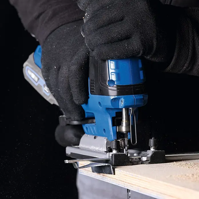 Scheppach IXES 20V Akku-Stichsäge BC-JS254-X - 20 V, Ohne Akku, Leerlaufhubzahl: 0 /min - 3.000 /min - Nahaufnahme einer Stichsäge in Aktion, die durch ein Holzbrett schneidet, bedient von einer Person mit Handschuhen.