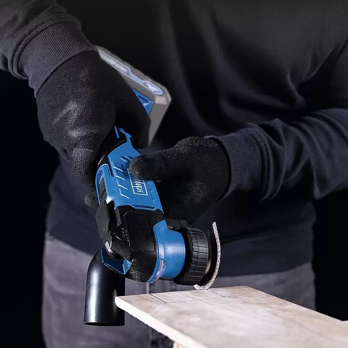 Scheppach IXES 20V Akku-Multitool C-MT40-X - 20 V - Person in schwarzen Handschuhen verwendet ein blau-schwarzes oszillierendes Multifunktionswerkzeug, um eine helle Fliese mit Bleistiftmarkierungen zu schneiden.