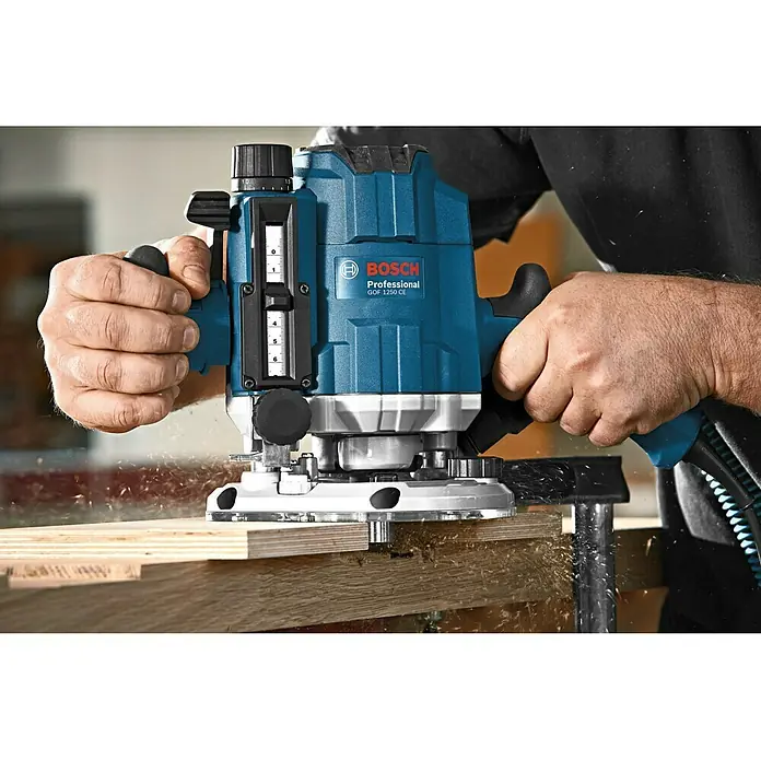 Bosch Professional Oberfräse GOF 1250 CE - 1.250 W, 60 mm - Bild einer Bosch Gof 1250 CE Oberfräse im Einsatz, ideal für präzise Holzarbeiten. Das Werkzeug ist blau und wird von einer Person bedient.