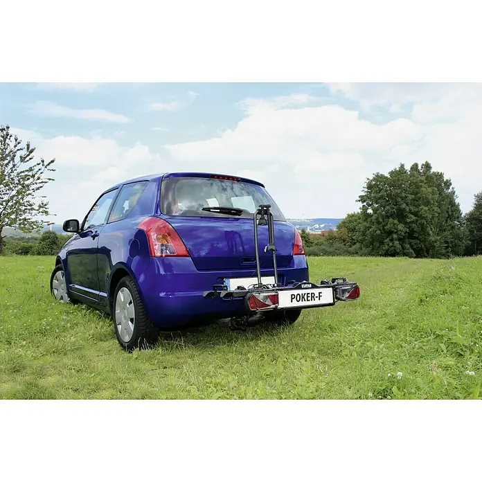 Eufab Portabicicletas Poker-F - Apto para: 2 bicicletas, Capacidad de carga: 60 kg, Específico para: Vehículos con enganche para remolque - El portabicicletas Eufab Poker-F está montado en un coche azul en un campo verde, ofreciendo un transporte seguro para bicicletas.