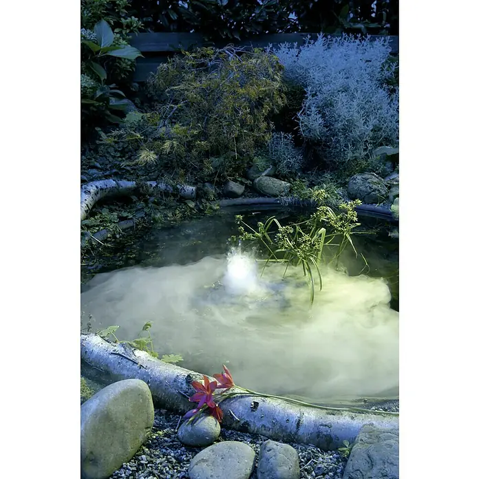 Ubbink Vernebler MystMaker III outdoor - Geeignet für: Gartenteiche, 60 W - Mystischer Teich mit Nebel, umgeben von Steinen, Pflanzen und einer umgestürzten Birkenrinde. Rote Blumen schmücken den Teichrand.