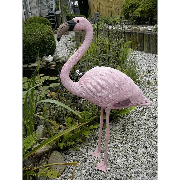 Ubbink Dekofigur Flamingo - 24 x 58 x 91,5 cm, Polyresin - Eine pinkfarbene Flamingo-Gartenfigur steht inmitten einer üppigen Gartenszene mit Pflanzen, Steinen und einem Teich, der eine verspielte Note verleiht.