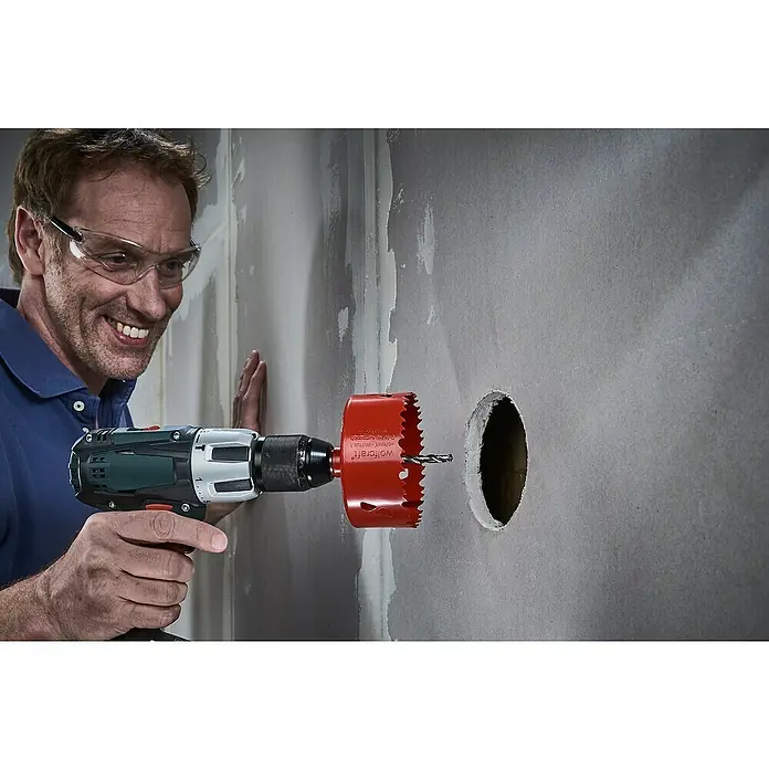 Wolfcraft Lochsäge - Arbeitsdurchmesser: 100 mm, Schnitttiefe: 40 mm - Ein Mann bohrt mit einer Lochsäge ein Loch in eine Wand. Die Lochsäge ist rot und am Bohrer befestigt. Schutzbrille wird getragen.