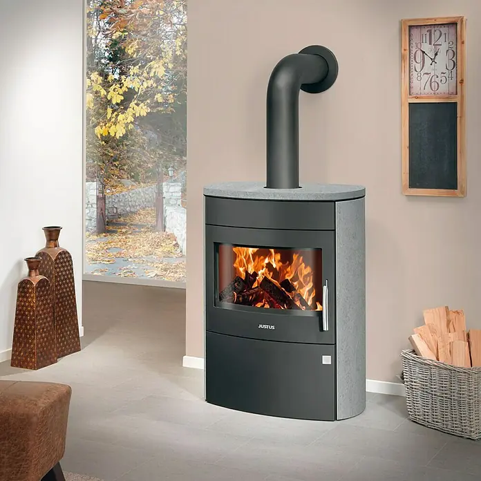 Justus Kaminofen Agero 2.0 - 7 kW, Raumheizvermögen: 144 m³, Material Verkleidung: Speckstein, Schwarz - Nahaufnahme eines Justus-Kaminofens mit Holzfeuer, der Wärme und Gemütlichkeit in den Raum bringt.