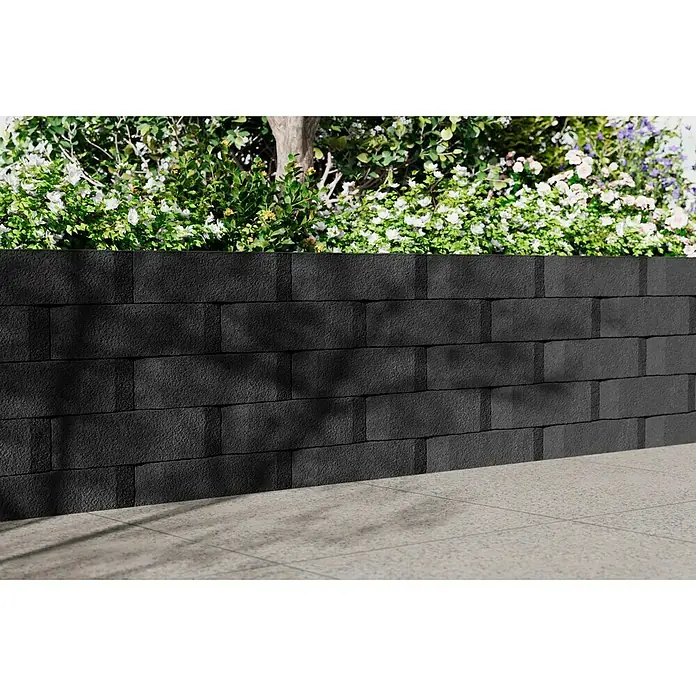 Christoph Mauerstein Antikblock - 30 x 15 x 7,5 cm, Anthrazit, Beton - Nahaufnahme einer schwarzen Mauer mit darauf wachsenden Pflanzen, die sich ideal für die Gartengestaltung eignet.