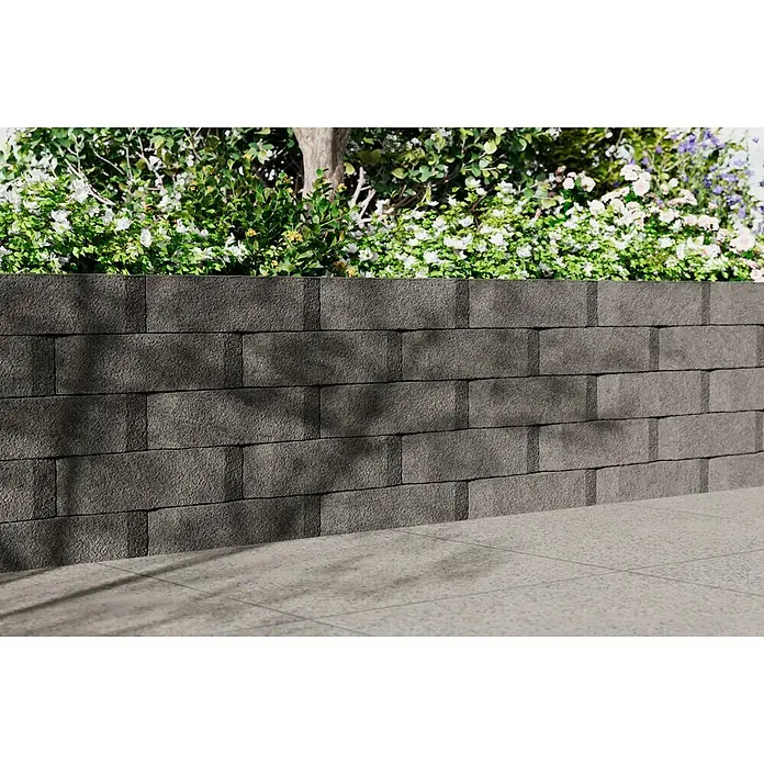 Christoph Mauerstein Antikblock - 30 x 15 x 7,5 cm, Grau, Beton - Eine graue Mauer aus Betonsteinen stützt einen Garten mit Pflanzen und Blumen, die über die Kante wachsen. Schattenmuster auf der Mauer.