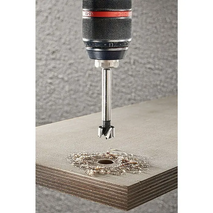 Wolfcraft Forstnerbohrer - Durchmesser Bohrer: 15 mm - Nahaufnahme eines Forstnerbohrers, der ein präzises Loch in ein Holzbrett bohrt, umgeben von Holzspänen.