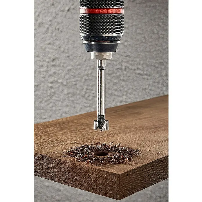 Wolfcraft Forstnerbohrer - Durchmesser Bohrer: 15 mm - Nahaufnahme einer Bohrmaschine mit Forstnerbohrer, die ein Loch in ein Holzbrett bohrt, Späne liegen herum.