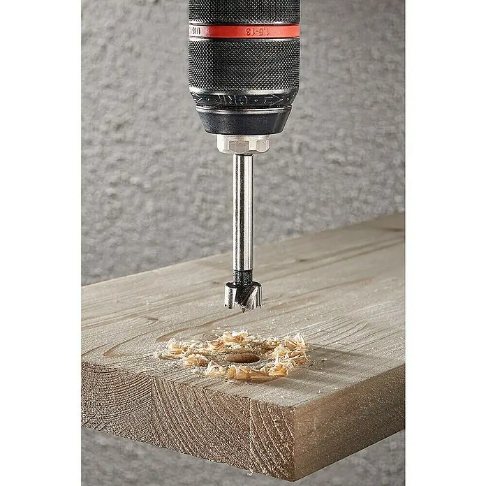 Wolfcraft Forstnerbohrer - Durchmesser Bohrer: 15 mm - Das Bild zeigt einen Forstnerbohrer, der ein sauberes Loch in ein Holzbrett bohrt, umgeben von Holzspänen.