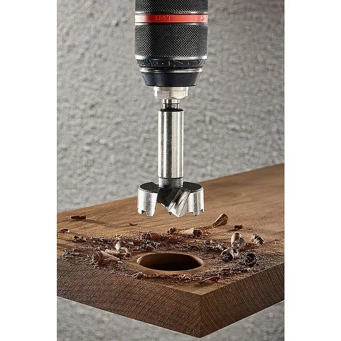 Wolfcraft Forstnerbohrer - Durchmesser Bohrer: 40 mm - Forstnerbohrer, eingesetzt in eine Bohrmaschine, bohrt ein Loch in ein Holzbrett, umgeben von Holzspänen.