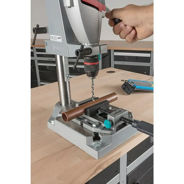 Wolfcraft Mordaza de sujeción - Anchura de sujeción: 80 mm - Un taladro de columna Wolfcraft perfora un tubo de cobre, que está asegurado en un tornillo de banco sobre un banco de trabajo.