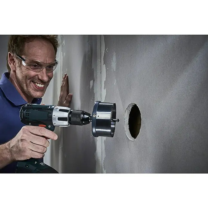 Wolfcraft Mehrkranzlochsäge - 5 -tlg., Arbeitsdurchmesser: 60 mm - 95 mm, Schnitttiefe: 40 mm - Ein Mann bohrt mit einer Lochsäge ein Loch in eine Wand, Schutzbrille und Bohrmaschine im Fokus.