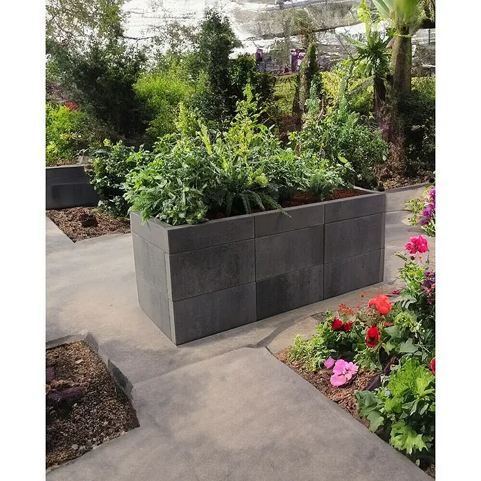 EHL Creaform Pflanzkübel - 188 x 67 x 75 cm, Lavaschwarz, Rechteckig, Beton - Rechteckiger Pflanzkasten aus Betonblöcken mit üppigen grünen Pflanzen, eingebettet in einen schön angelegten Gartenbereich mit Betonplatten.