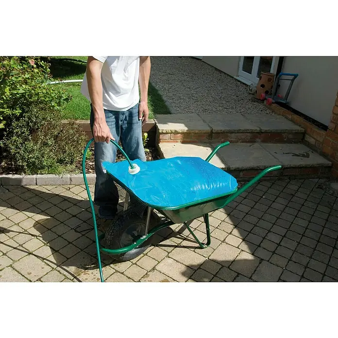 Kerbl Wasserbehälter für Schubkarren H2GOBAG - L x B x H: 33 x 24,5 x 6 cm, Fassungsvermögen: 80 l - Ein Mann befüllt eine grüne Schubkarre mit einem blauen Wasserbehälter und einem grünen Schlauch auf einem gepflasterten Hof.