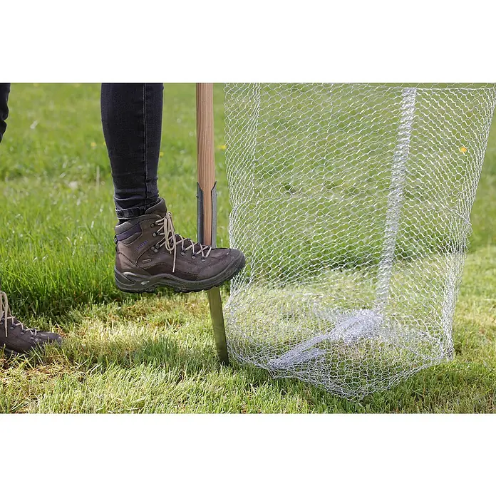 Kerbl Wühlmauskorb Klein - L x B x H: 35 x 35 x 40 cm - Nahaufnahme von einem Stiefel, der auf einen Holzpfosten mit Maschendraht tritt, auf einer Rasenfläche im Freien.