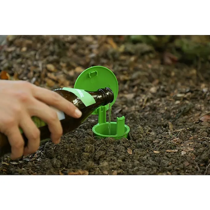 Kerbl Schneckenfalle Snail Bowl - L x B x H: 15,5 x 9 x 8,5 cm - Eine Person gießt Bier aus einer Flasche in einen grünen Erdlochtrichter, der im Boden steckt.