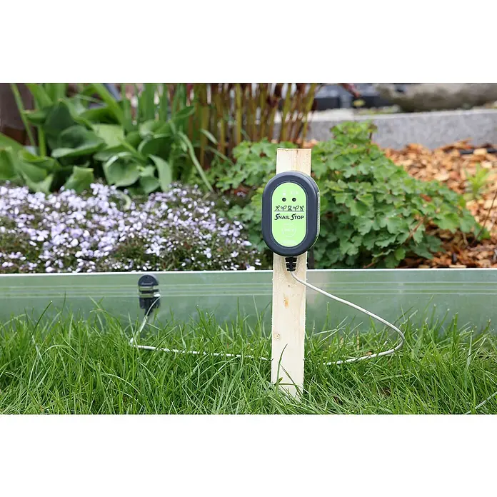 Kerbl Schneckenzaun Snail Stop - Länge: 10 m - Nahaufnahme eines Snail Stop-Geräts, das an einem Holzpfahl befestigt ist, mit einem Garten im Hintergrund.
