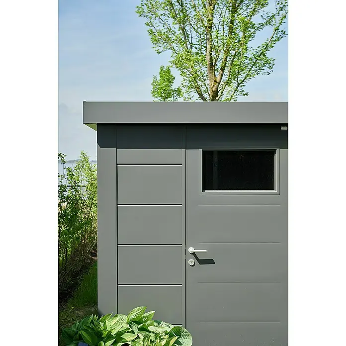 Telluria Metallgerätehaus Classico 2424 - Außenmaß inkl. Dachüberstand (B x T): 258 x 258 cm, Stahl, Anthrazit, Ohne Set - Ein graues Gartenhaus mit Tür und Fenster. Es steht vor einem grünen Hintergrund aus Büschen und einem Baum. Die Tür hat einen Griff und ein Schloss.