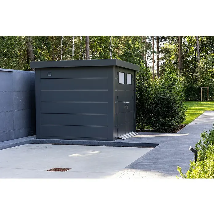 Telluria Metallgerätehaus Classico 3030 - Außenmaß inkl. Dachüberstand (B x T): 318 x 318 cm, Stahl, Anthrazit, Ohne Set - Das Bild zeigt ein modernes, anthrazitfarbenes Gartenhaus mit Flachdach neben einer gepflasterten Fläche und üppigem Grün.