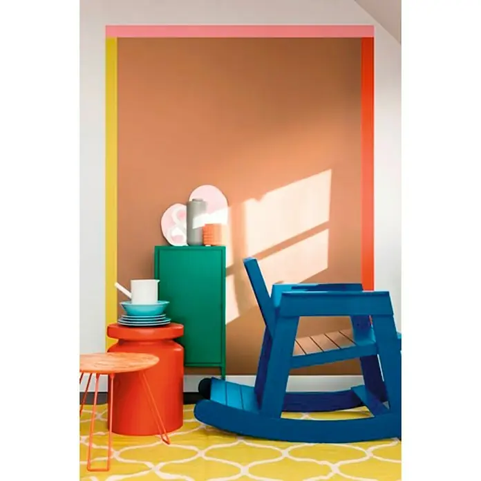 Bruguer Esmalte de color Acrylic Multisuperficie - Verde Galicia, Satinado, 750 ml, Base de agua - Interior colorido con una mecedora azul, una mesa naranja y un mueble verde contra una pared vibrante. Los muebles añaden acentos vivos al espacio.