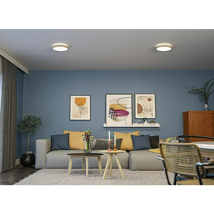 Paulmann LED-Panel rund Cosara - 15 W, Ø x H: 30 x 6,2 cm, Beige, Neutralweiß - Ein Wohnzimmer mit modernen Deckenleuchten, die ein warmes Licht verbreiten und die blaue Wand hervorheben.