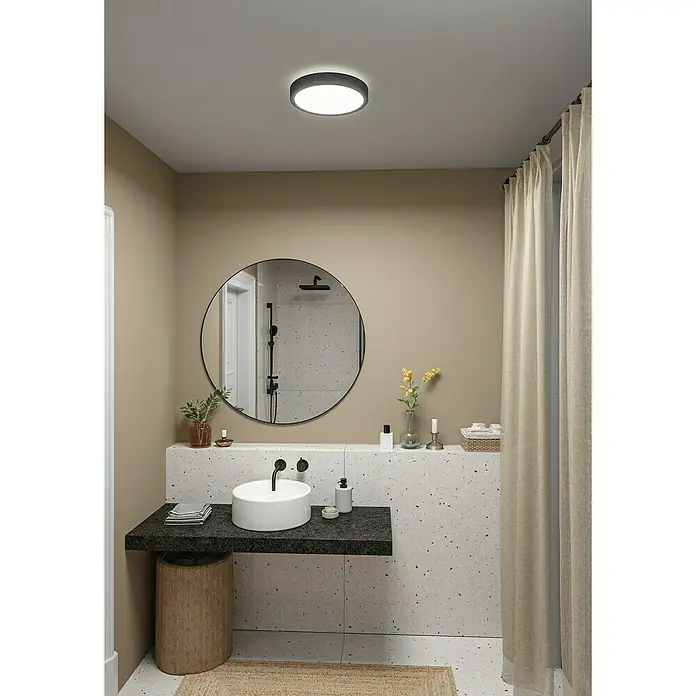Paulmann LED-Panel rund Cosara - 15 W, Ø x H: 30 x 6,2 cm, Dungelgrau, Warmweiß - Badezimmer-Interieur mit einem runden Spiegel über einem Waschbecken und einer modernen Deckenleuchte, die das Gesamtbild aufwertet.